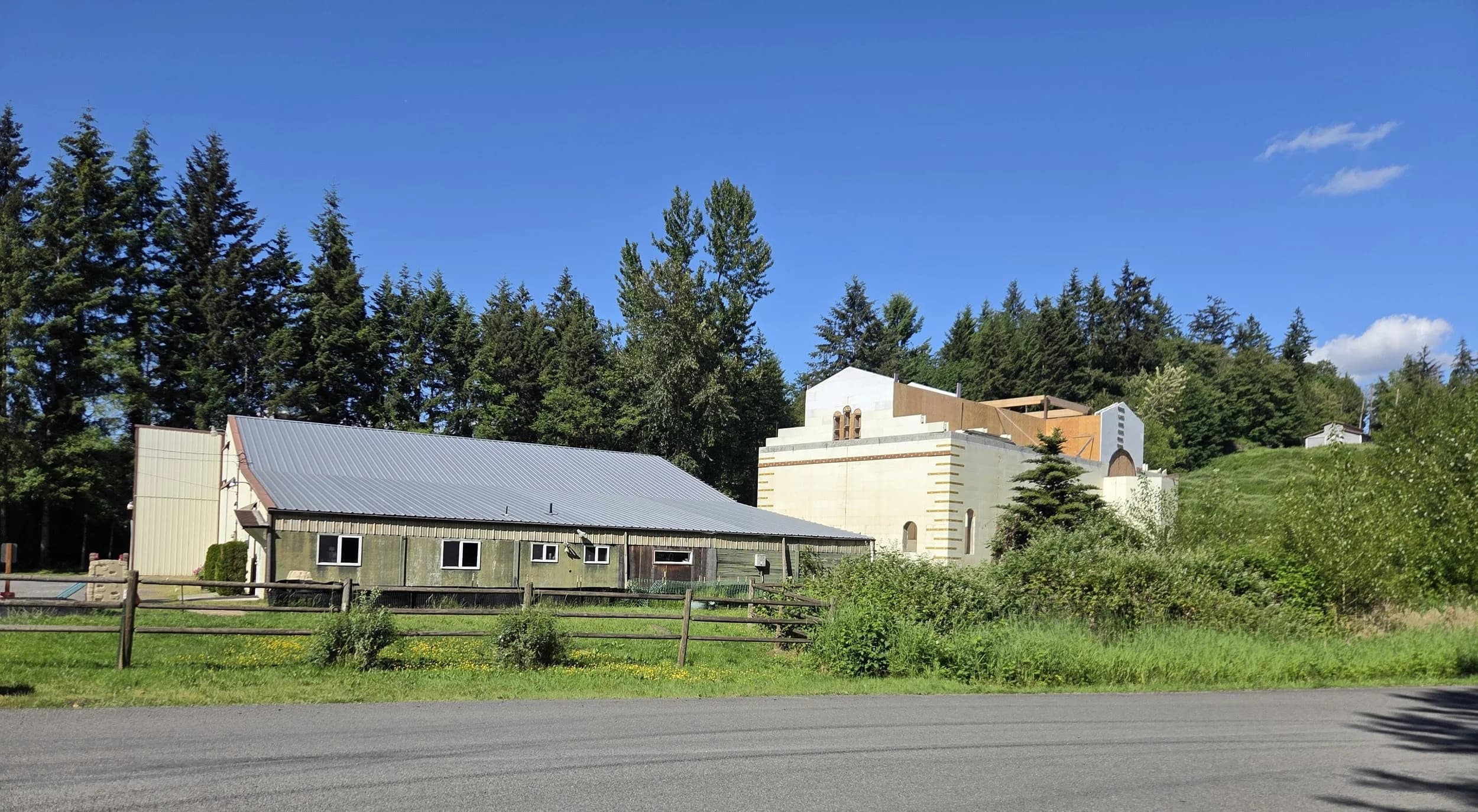 Wide roadside view of the existing parish building and unfinished concrete-block church.