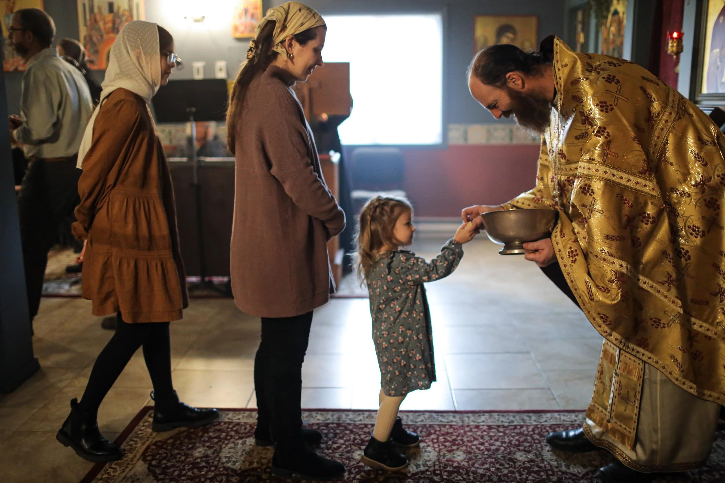 Orthodox priest offering blessed bread to a child after a service.